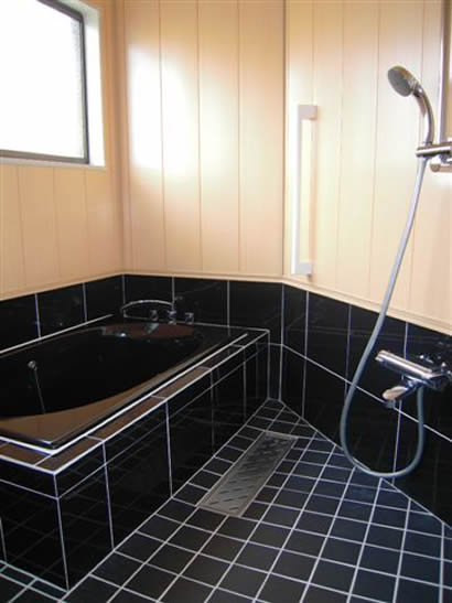 浴槽はポリエステル系人造大理石で一回り大きくなりました。黒の浴槽と腰タイルがかっこいいです。腰上の壁はバスパネルです。またぎ寸法を抑えた親切設計、これで腰を掛けて安定姿勢で入浴できます。